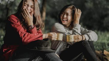 two women holding cups laughing at each other