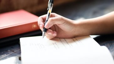 a person writing on a piece of paper with a pen